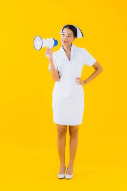 Asyalı güzel bir kadının portresi klinikte ve hastanede iletişim kurmak için megafonlu Taylandlı hemşire ve sarı izole bir arka plan.