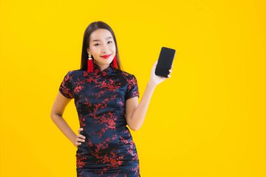 Güzel bir portre genç Asyalı kadın Çin elbisesi giyer Çin 'in yeni yıl konsepti için sarı izole edilmiş arka planda akıllı cep telefonu kullanır.