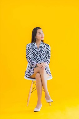 Güzel bir Asyalı kadın, sarı izole edilmiş arka planda hareketli bir şekilde sandalyede oturuyor.