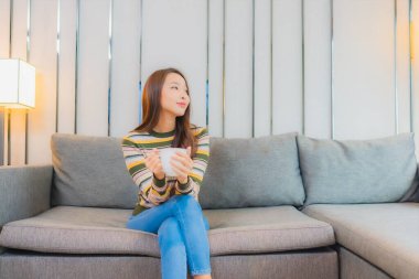 Güzel bir Asyalı kadın portresi. Oturma odasındaki kanepede rahatça gülümse.