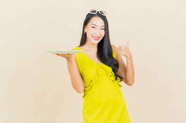 Güzel Asyalı bir kadının portresi. Arka planda boş tabak tabağıyla gülümsüyor.