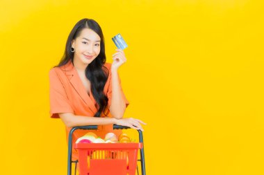 Asyalı güzel bir kadının portresi. Sarı arka planda süpermarketten alınmış alışveriş sepetiyle gülümsüyor.