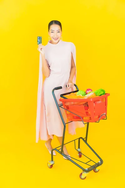 노란색 배경에 슈퍼마켓에서 식료품 바구니를 가지고 아름다운 아시아 여자의 — 스톡 사진