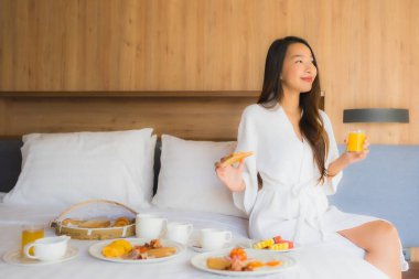 Güzel bir Asyalı kadın portresi. Yatak odasındaki iç kısımda kahvaltıdan zevk alıyor.