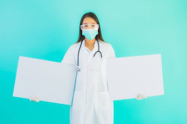 Mavi izole edilmiş arka planda boş ilan panosuyla güzel Asyalı doktor kadın portresi.