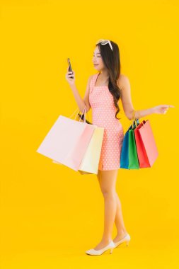 Renkli alışveriş çantalı güzel Asyalı kadın akıllı cep telefonu ve sarı izole edilmiş arka planda kredi kartı.