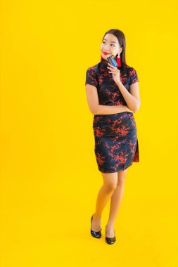 Güzel bir Asyalı kadın portresi. Sarı izole edilmiş arka planda Çin elbisesi, kredi kartı ve akıllı cep telefonu takıyor.