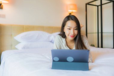 Güzel bir Asyalı kadının portresi yatak odasının içinde kredi kartıyla tablet kullanıyor.