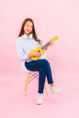 Portrait beautiful young asian woman play ukulele on pink color isolated background