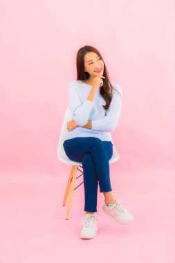 Portrait beautiful young asian woman sit on chair with pink color background