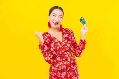 Sarı izole edilmiş arka planda alışveriş yapmak için güzel bir Asyalı kadın kredi kartı.
