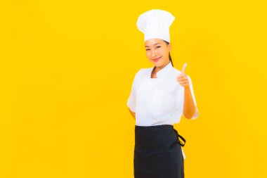 Güzel bir Asyalı kadın portresi ya da sarı izole arkaplanda şapkası olan aşçı üniforması.