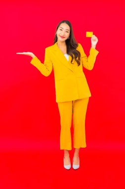 Güzel bir Asyalı kadının portresi kırmızı arka planda kredi kartıyla cep telefonu kullanıyor.