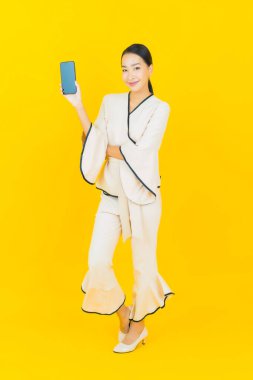 Sarı arka planda akıllı cep telefonlu güzel genç Asyalı kadın portresi.
