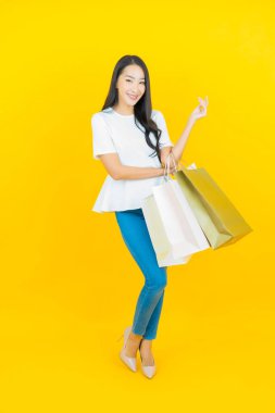 Sarı arka planda alışveriş çantasıyla gülümseyen güzel Asyalı kadın portresi