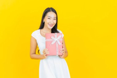 Asyalı güzel bir kadının portresi. Sarı arka planda kırmızı hediye kutusuyla gülümsüyor.