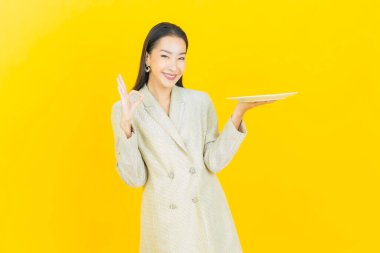 Güzel Asyalı bir kadının portresi. Arka planda boş tabak tabağıyla gülümsüyor.