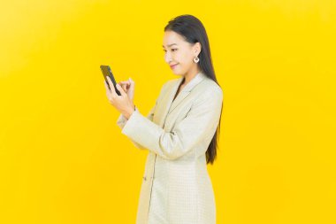 Renkli arka planda akıllı cep telefonuyla güzel Asyalı kadın gülümsemesi