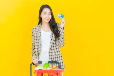 Renkli arka planda süpermarketten alınmış market sepetiyle gülümseyen güzel Asyalı kadın portresi.