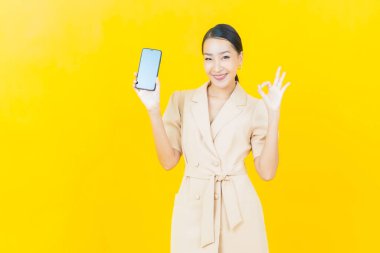 Renkli arka planda akıllı cep telefonuyla güzel Asyalı kadın gülümsemesi