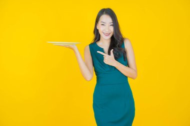 Güzel Asyalı bir kadının portresi. Arka planda boş tabak tabağıyla gülümsüyor.