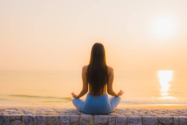 Genç Asyalı kadının portresi sağlık için gün doğumunda deniz kıyısı okyanusunda meditasyon yapıyor.