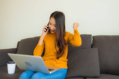 Laptop bilgisayar kullanan Asyalı genç bir kadının portresi. Akıllı cep telefonu ve kahve fincanı olan bir defter.