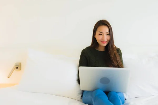 在卧室内带着手提电脑和咖啡杯在床上工作的漂亮年轻亚洲女人的画像 — 图库照片