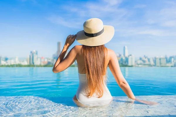 Asyalı güzel bir kadının portresi gülümsüyor şehir manzaralı açık havuz etrafında rahatça yüzüyor.