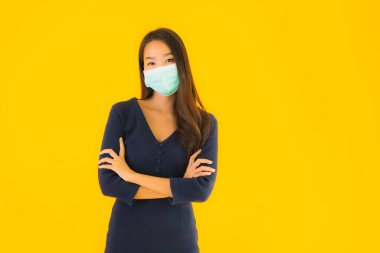 Koronavirüsten korunmak için maske takmış güzel Asyalı bir kadın portresi ve sarı izole edilmiş arka planda 19 numara.
