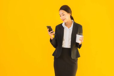 Portre güzel genç Asyalı kadın akıllı cep telefonu ve kahve fincanı ile izole edilmiş sarı arka planda