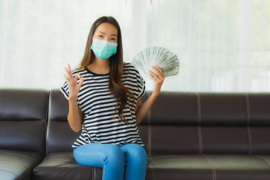 Maskeli güzel Asyalı kadının portresi evde para ya da para gösteriyor.