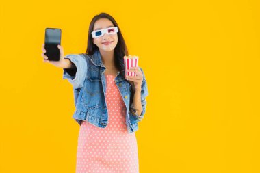 Güzel bir Asyalı kadın portresi telefon patlamış mısırı ve sarı izole edilmiş bir arka planda film izlemekten memnun.