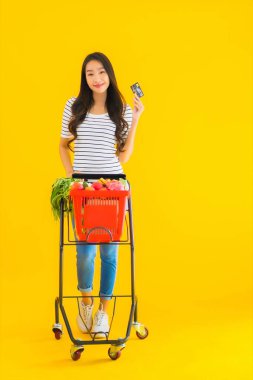 Marketten alışveriş yapan güzel Asyalı kadın portresi. Sarı izole edilmiş arka planda kredi kartıyla.