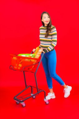 Marketten aldığı alışveriş sepetiyle kırmızı izole arka planda güzel bir Asyalı kadın portresi.