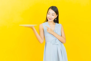 Güzel Asyalı bir kadının portresi. Arka planda boş tabak tabağıyla gülümsüyor.