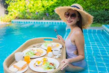 Genç Asyalı kadının portresi mutlu bir gülümseme ile otel havuzunda yüzen kahvaltı tepsisinin keyfini çıkar.