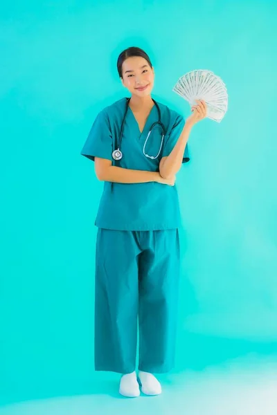 Portrait beautiful young asian doctor woman show money and cash on blue isolated background