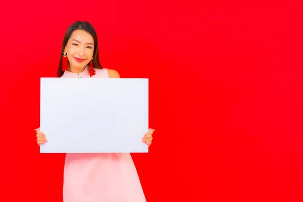 美丽的年轻亚洲女人在红色背景上展示白色的空广告牌 — 图库照片