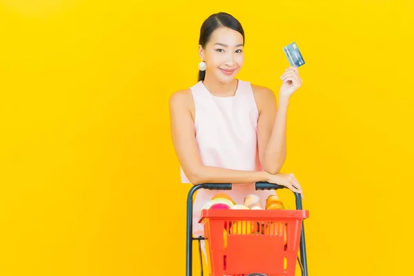 在黄色背景的超市里 年轻美丽的亚洲女人带着购物篮微笑 — 图库照片