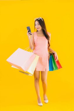 Renkli alışveriş çantalı güzel Asyalı kadın akıllı cep telefonu ve sarı izole edilmiş arka planda kredi kartı.