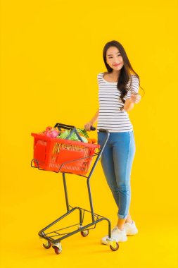 Sarı izole edilmiş arka planda, süpermarketten alışveriş sepeti taşıyan güzel Asyalı kadın portresi