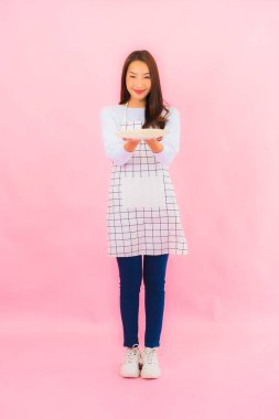 Portrait beautiful young asian woman in kitchen wear with apron on pink isolated background