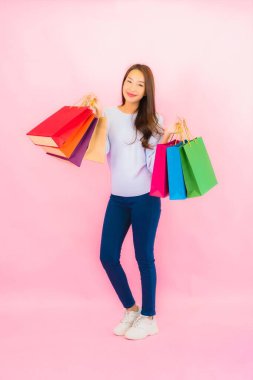 Portrait beautiful young asian woman with colorful shopping bag on pink color isolated background
