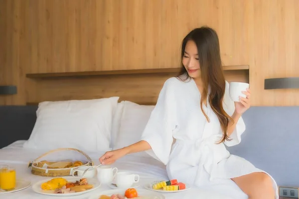 肖像画美しい若いアジアの女性幸せな楽しみますベッドルームのインテリアでベッドの上の朝食 — ストック写真