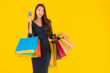 Portre güzel genç Asyalı kadın alışveriş çantası kredi kartı ve akıllı cep telefonu sarısı izole bir arka plan.