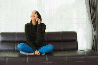 Güzel bir Asyalı kadın oturma odasındaki koltukta akıllı cep telefonu ya da cep telefonu kullanıyor.