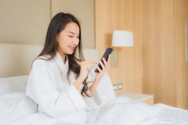 Yatak odasının içinde akıllı cep telefonlu güzel Asyalı kadın portresi.