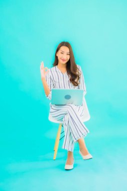 Güzel bir Asyalı kadın portresi bilgisayar bilgisayarı kullanıyor ve mavi izole edilmiş arka planı olan bir sandalyeye oturuyor.