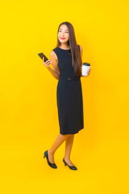 Kahve fincanı ve sarı arka planda akıllı cep telefonlu güzel Asyalı iş kadını portresi.